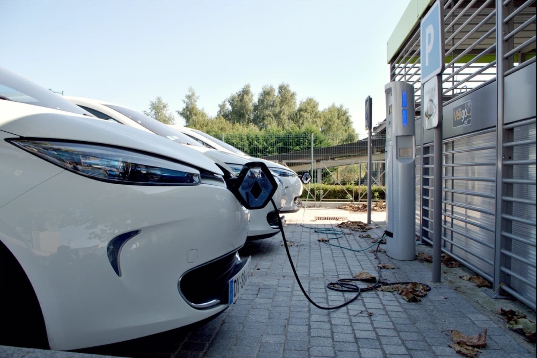 A row of white electric cars plugged into a charging post in a car park.